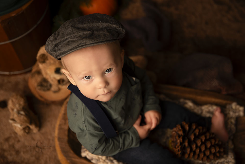 A baby boy in a chapped hat sits for a portrait in a autumn woodland scene with Simply Shelayna Baby Photography in Syracuse NY.