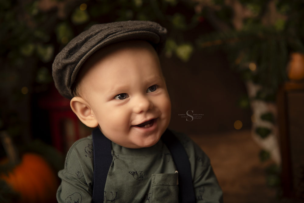 A baby boy in a chapped hat sits for a portrait in a autumn woodland scene with Simply Shelayna Baby Photography in Syracuse NY.