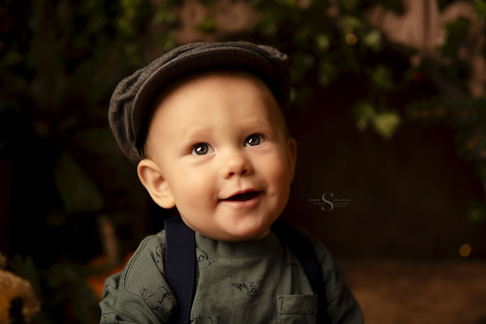 A baby boy in a chapped hat sits for a portrait in a autumn woodland scene with Simply Shelayna Baby Photography in Syracuse NY.