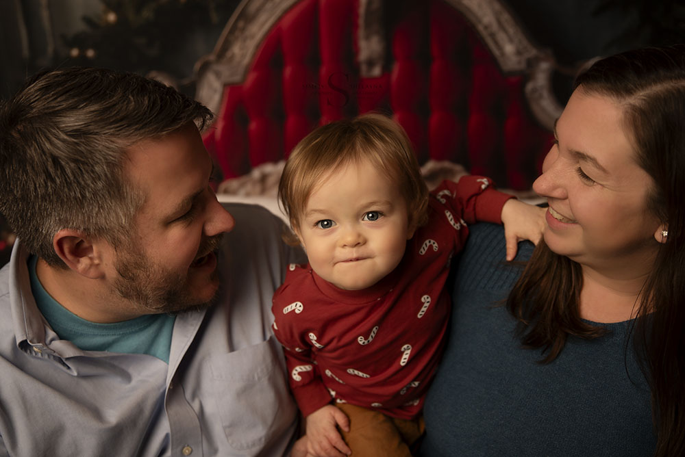 A family of 3, dressed in coordinating Christmas pjs, pose for a Night Before Christmas portrait with Simply Shelayna family photographer in Oswego NY.