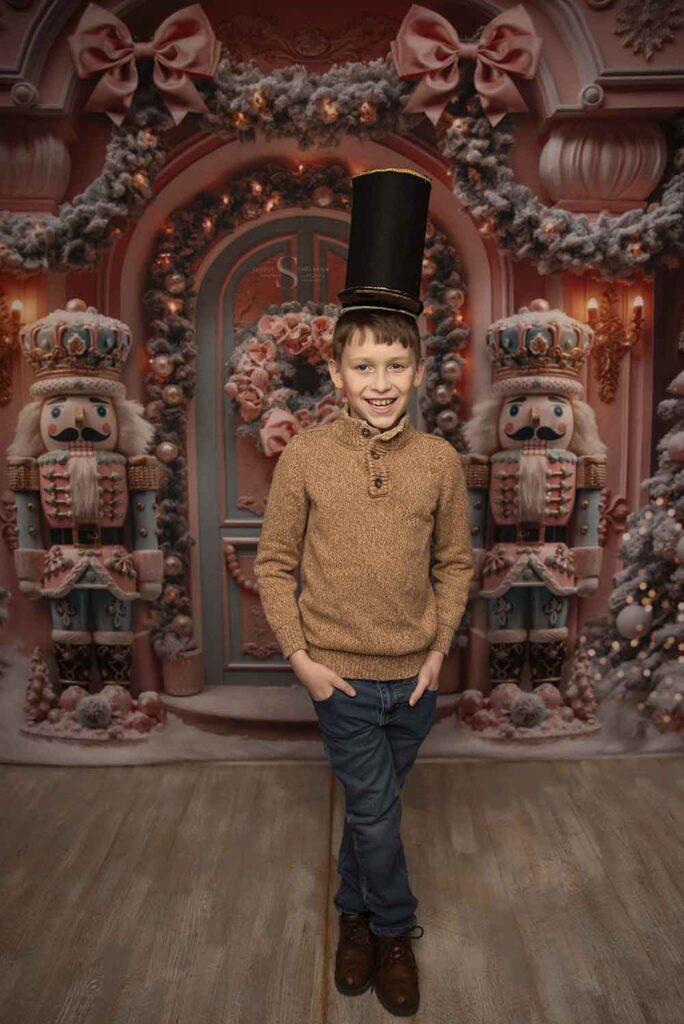 A young boy stands erect with a nutcracker hat tall upon his head for a Christmas portrait with Simply Shelayna Family Photography in Oswego NY.
