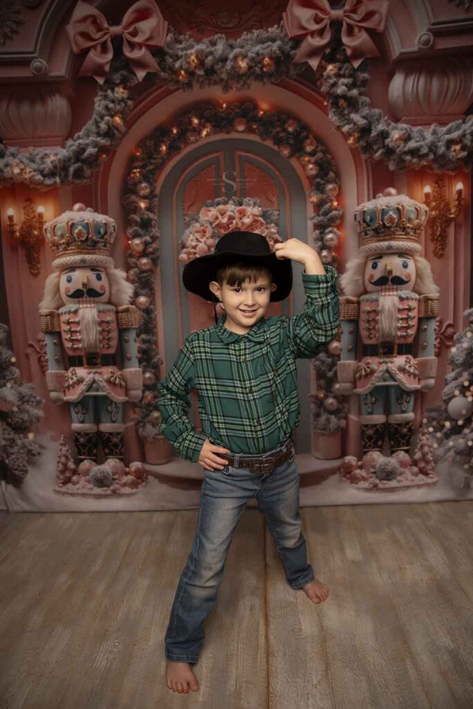 A young boy in a cowboy hat poses in a pink nutcracker scene with Simply Shelayna Family Photography in CNY.