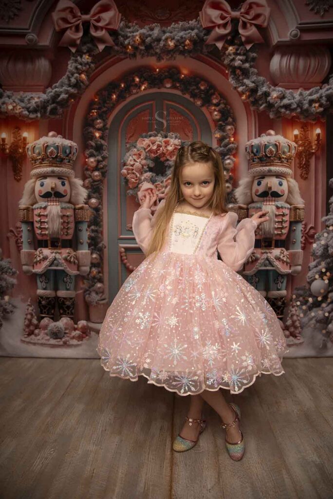 A young girl poses for the camera in a pink nutcracker dress for Christmas portraits with Simply Shelayna Family photography in Syracuse NY.