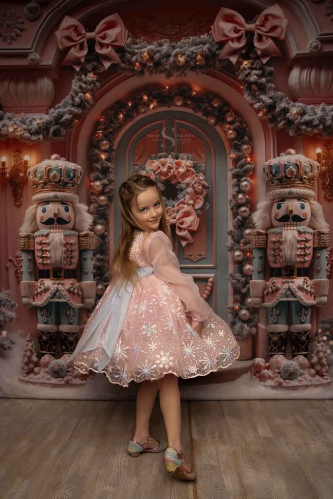 A young girl poses for the camera in a pink nutcracker dress for Christmas portraits with Simply Shelayna Family photography in Syracuse NY.