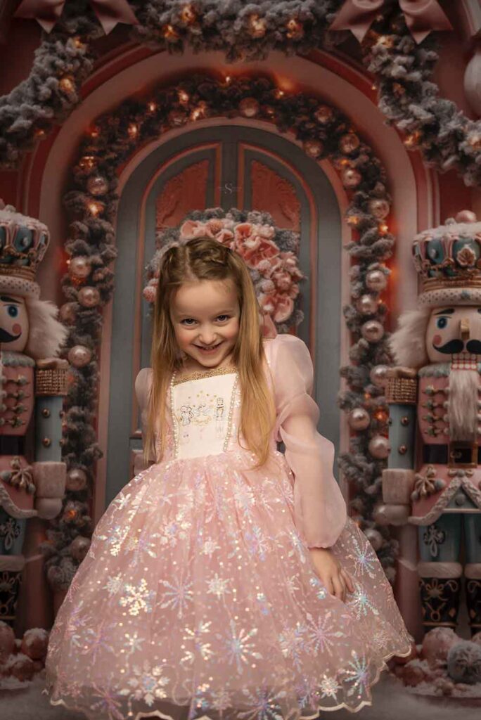 A young girl poses for the camera in a pink nutcracker dress for Christmas portraits with Simply Shelayna Family photography in Syracuse NY.
