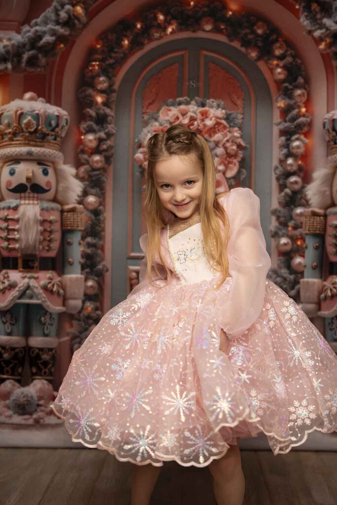 A young girl poses for the camera in a pink nutcracker dress for Christmas portraits with Simply Shelayna Family photography in Syracuse NY.
