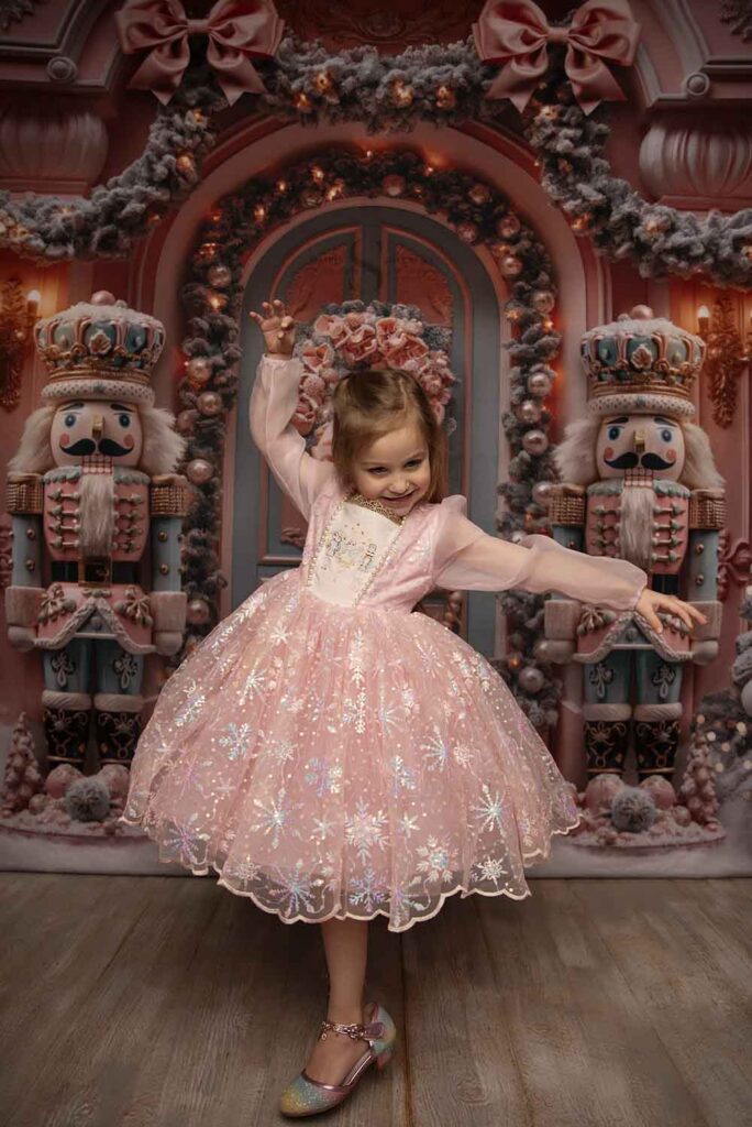 A young girl poses for the camera in a pink nutcracker dress for Christmas portraits with Simply Shelayna Family photography in Syracuse NY.