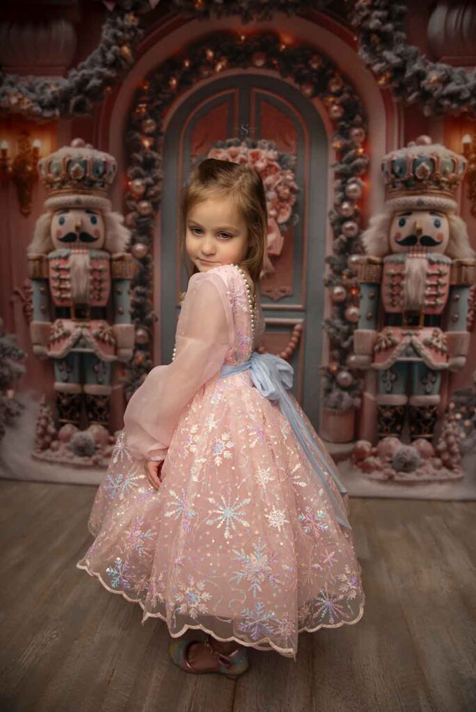 A young girl poses for the camera in a pink nutcracker dress for Christmas portraits with Simply Shelayna Family photography in Syracuse NY.