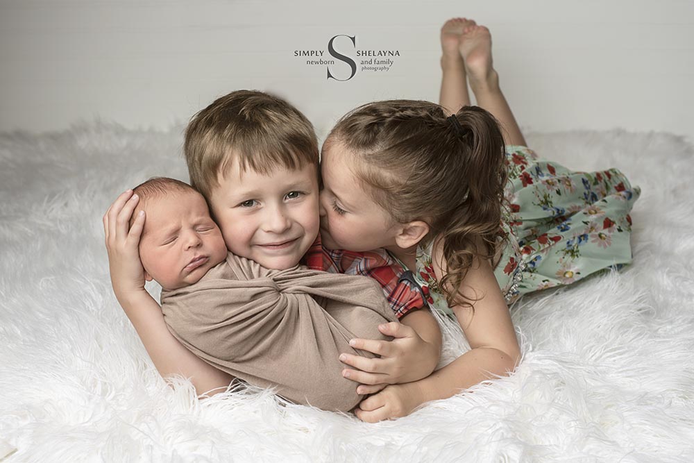 Two big siblings proudly hold their baby brother for a family portrait with Simply Shelayna Family Photography in CNY.