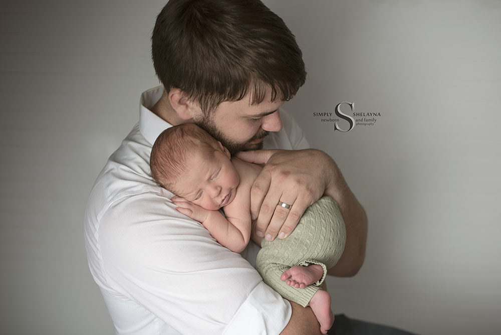 A father holds his newborn son up on his shoulder with Simply Shelayna Newborn Photography in Oswego NY.