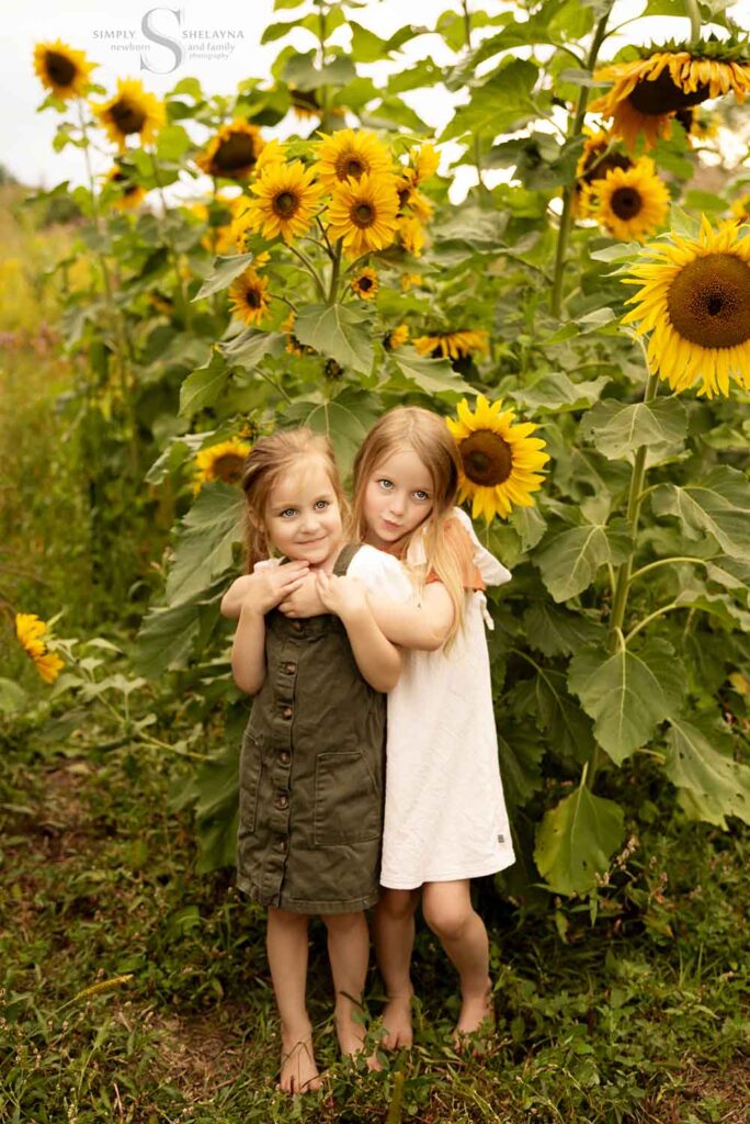 Two sisters pose in front of a sunflower field with Simply Shelayna Family Photography in CNY.
