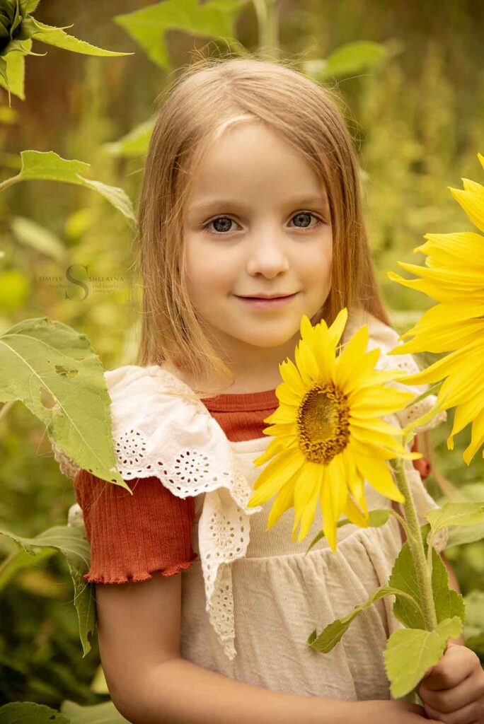 A young girl poses in a sunflower field with Simply Shelayna Family Photographer in CNY.