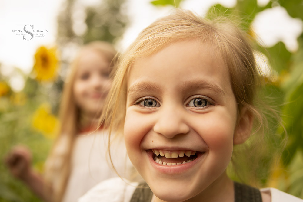 A young girl poses in a sunflower field with Simply Shelayna Family Photographer in CNY.