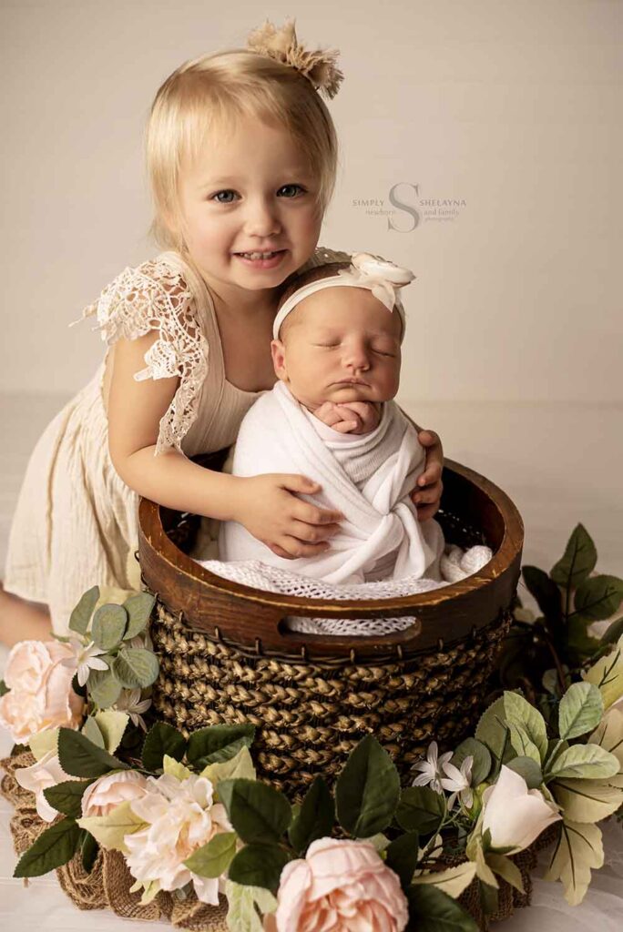 A big sister holds onto who wrapped in a bucket newborn sister for a sibling portrait with Simply Shelayna Newborn Photography in Syracuse NY.