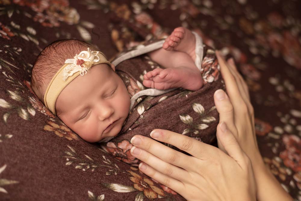 the hands of a mother are captured holding her wrapped baby pose on a posing bed with Simply Shelayna Newborn Photography in Oswego NY.