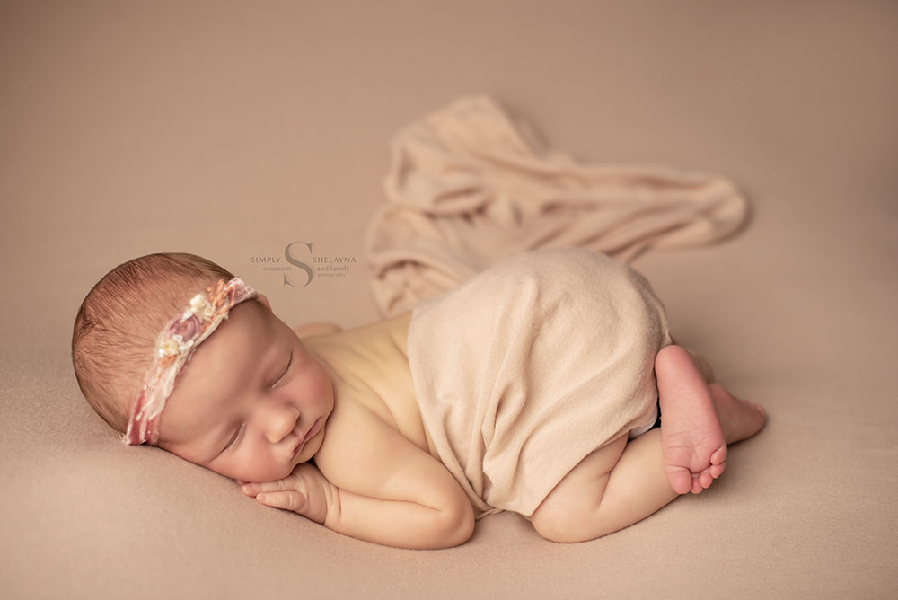 A newborn baby sleeps in bum up pose while a swaddled is draped over her bum with Simply Shelayna Newborn Photography in Syracuse NY.