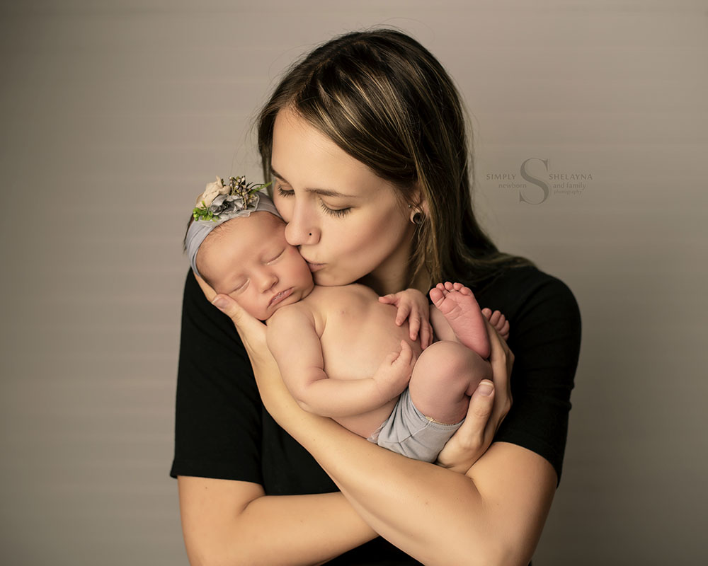 A mother tenderly kisses her newborn daughter with Simply Shelayna Newborn photography in CNY.
