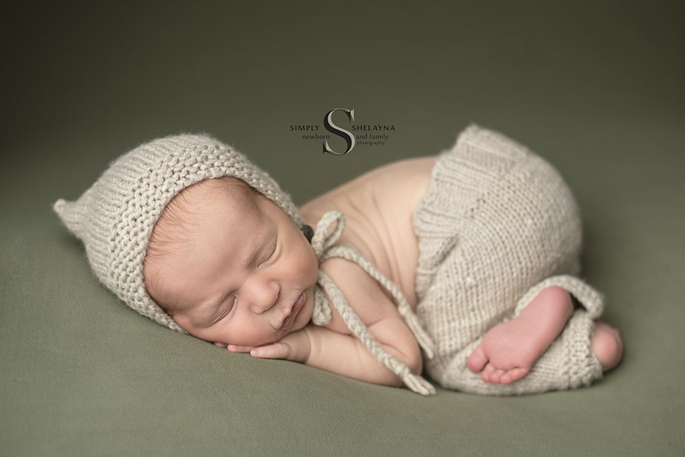 A newborn baby boy wears a handknitted bonnet and trousers while posed in Bum Up pose with Simply Shelayna Newborn Photography in Syracuse NY.