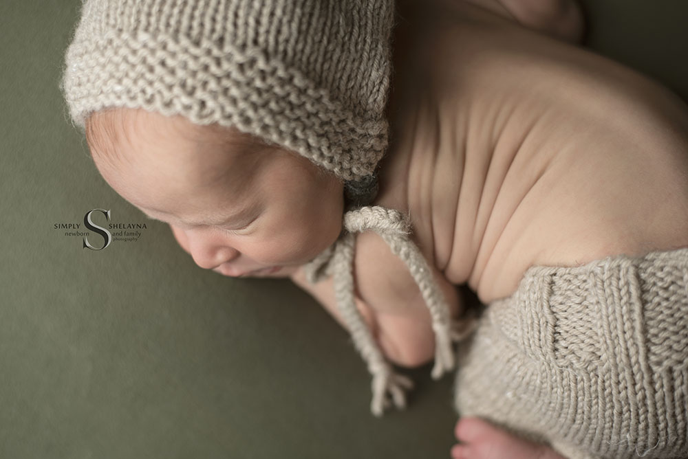 A newborn baby boy wears a handknitted bonnet and trousers while posed in Bum Up pose with Simply Shelayna Newborn Photography in Syracuse NY.