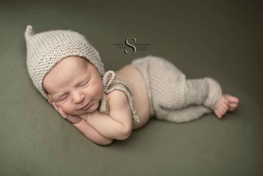 A newborn baby boy wears a handknitted bonnet and trousers while posed in side laying pose with Simply Shelayna Newborn Photography in Syracuse NY.