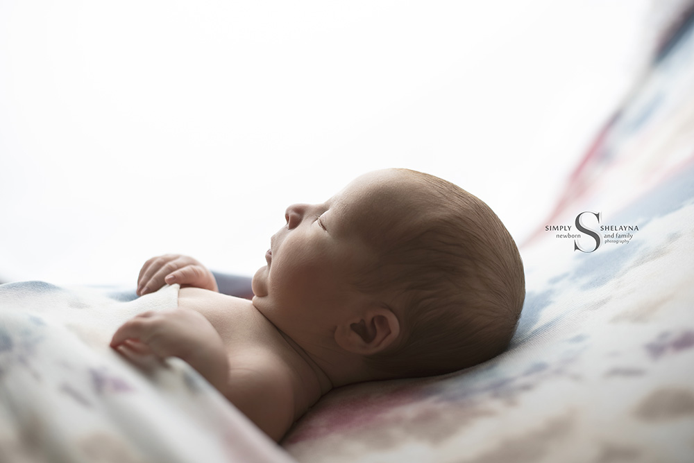 A newborn baby sleeps tucked in while a light from behind illuminates him with Simply Shelayna Newborn Photography in CNY.