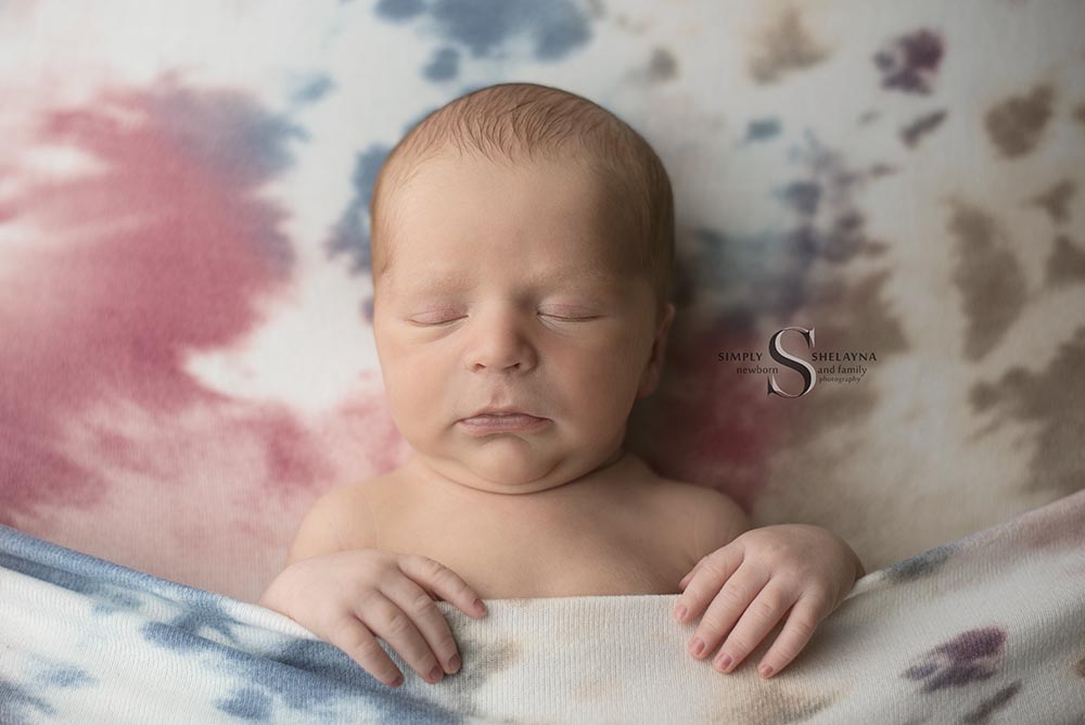 A newborn baby is tucked into a tie dyed blanket with Simply Shelayna Newborn photography in CNY.
