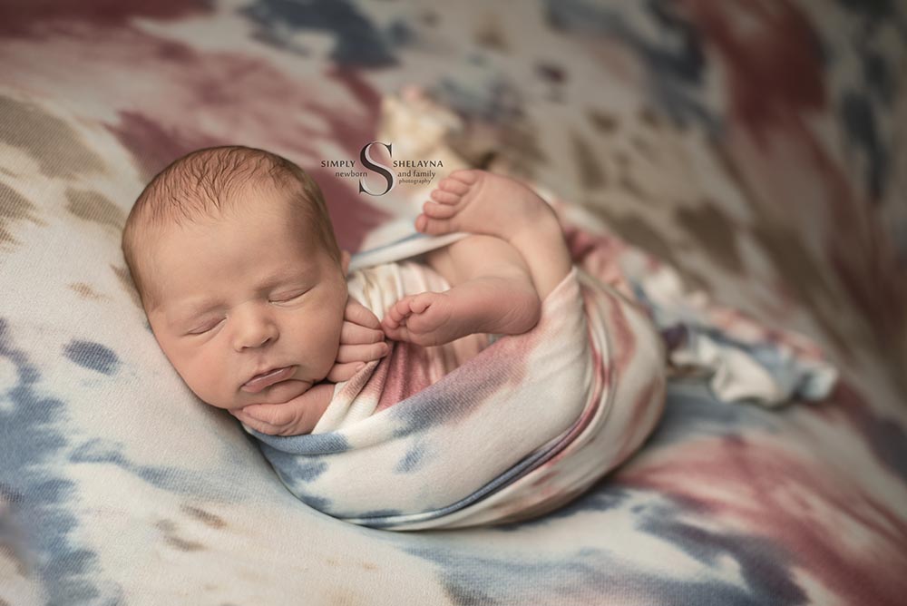 A baby boy is swaddled in a red, white, and blue wrap with Simply Shelayna Newborn Photography in Syracuse NY.