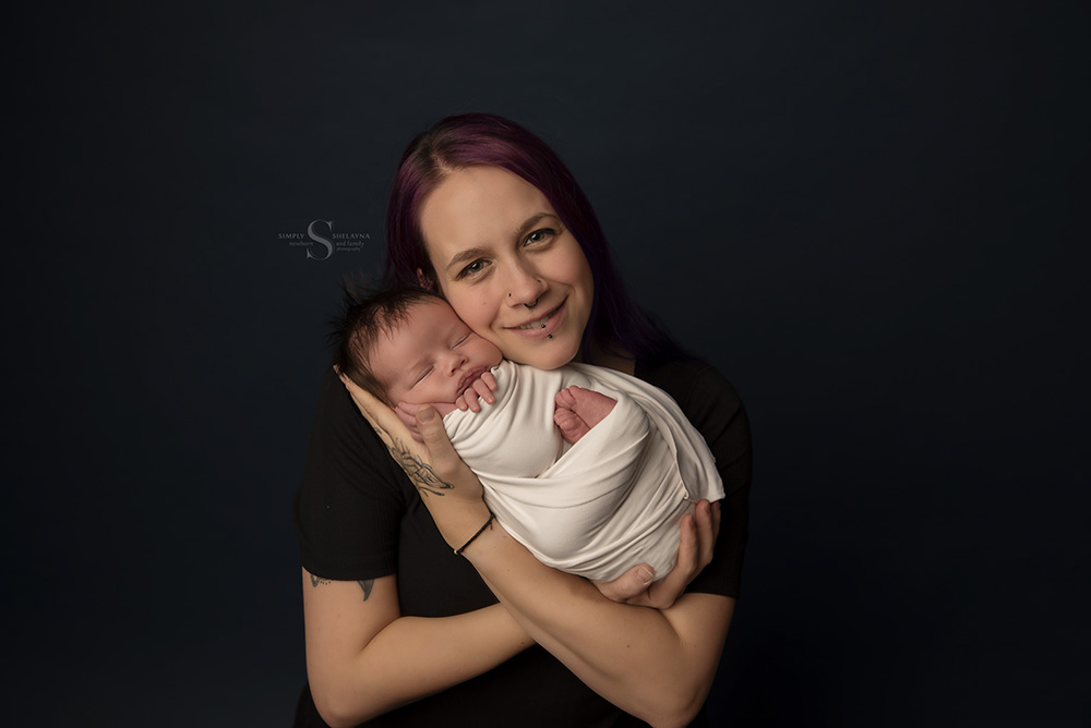 A mother embraces her son who is swaddled in a white wrap for a portrait with Simply Shelayna Newborn Photography in CNY.