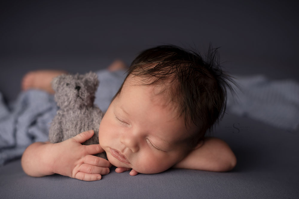 A newborn baby boy snuggles a teddy bear in chin up position pose with Simply Shelayna Newborn Photography in Syracuse NY.