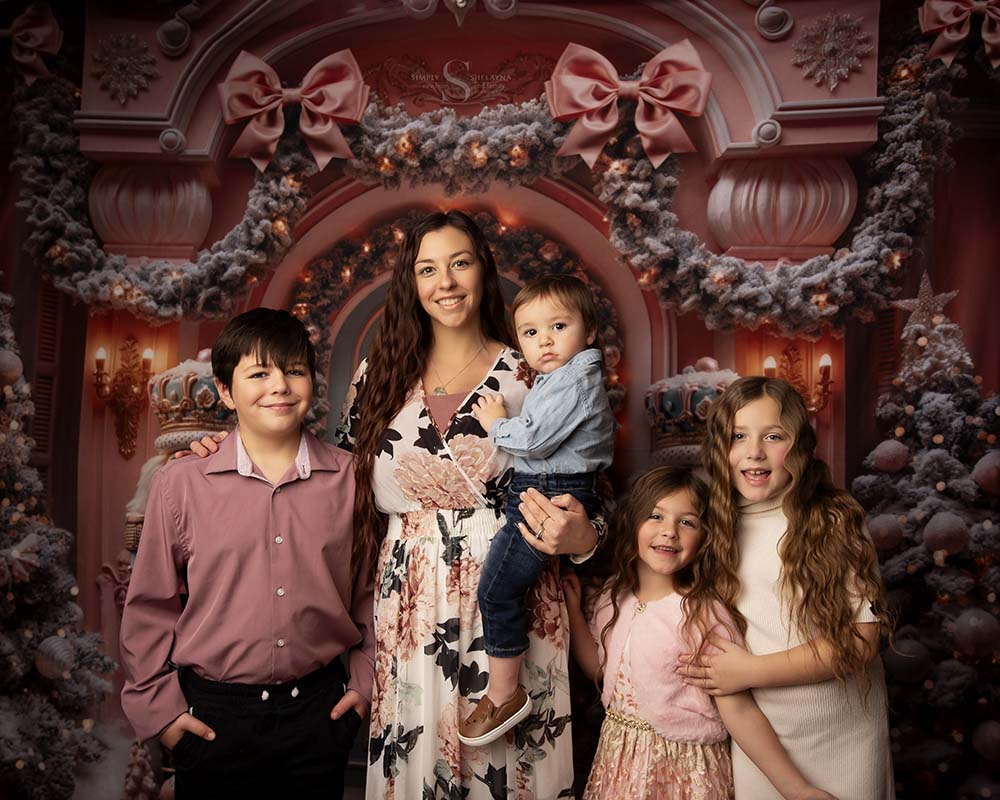 A mother and her four children pose in a front of a pink Christmas styled backdrop with Simply Shelayna Family Photography in Syracuse NY.