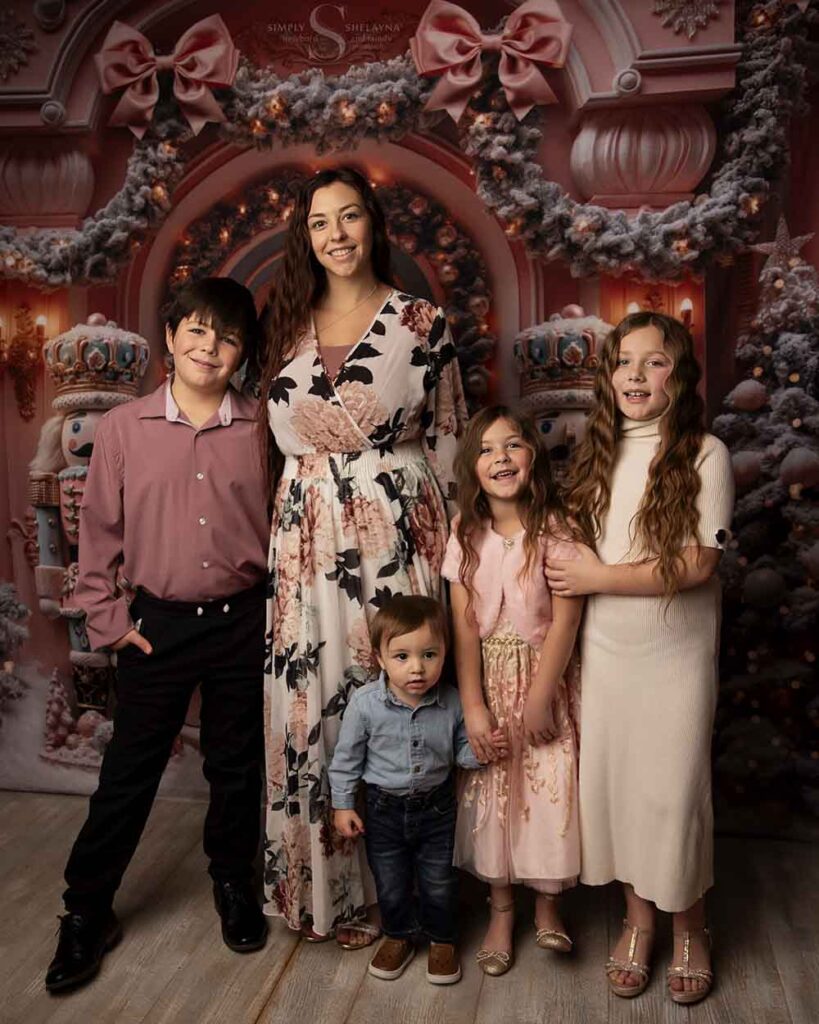 A mother and her four children pose in a front of a pink Christmas styled backdrop with Simply Shelayna Family Photography in Syracuse NY.