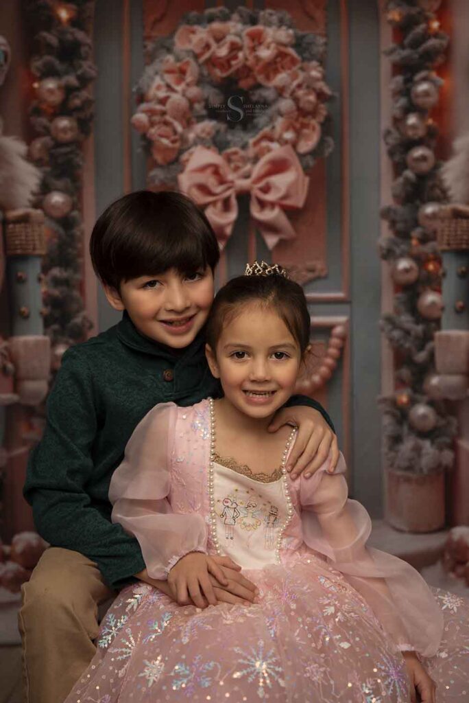A brother dressed in a green sweater hold his little sister, who is wearing a pink nutcracker ball gown with Simply Shelayna Family Photographer in Oswego NY.