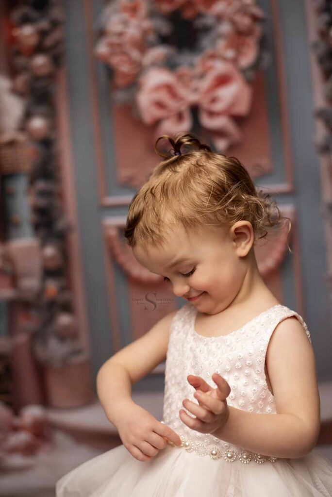 A young girl plays with the pearls on her white dress for a portrait with Simply Shelayna Child Photography in Albany NY.