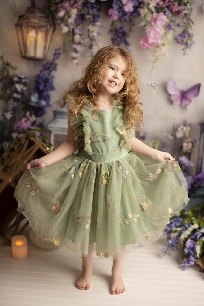 A five year old girl curtsies in a green butterfly dress with Simply Shelayna Child Photography in Oswego NY.