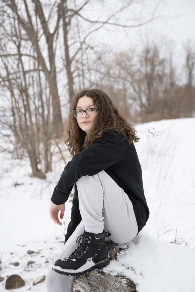A young man sits on the banks of Lake Ontario in a snow white seen for senior portraits with Simply Shelayna Photography in Oswego County NY.