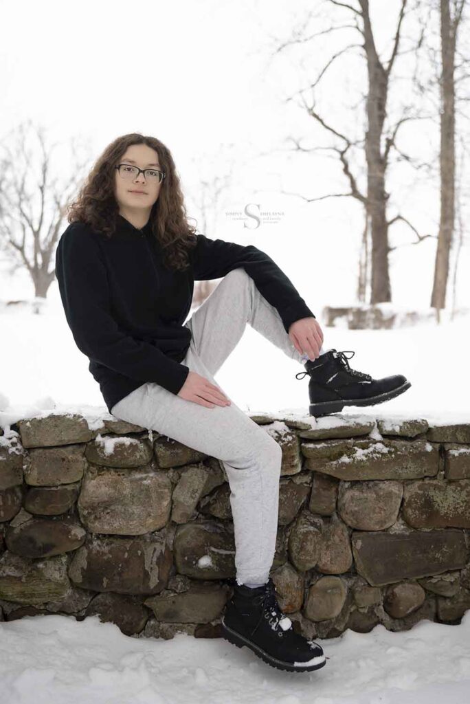 A high school senior sits upon a stone wall at Mexico Point State Park in CNY with Simply Shelayna Family Photographer.