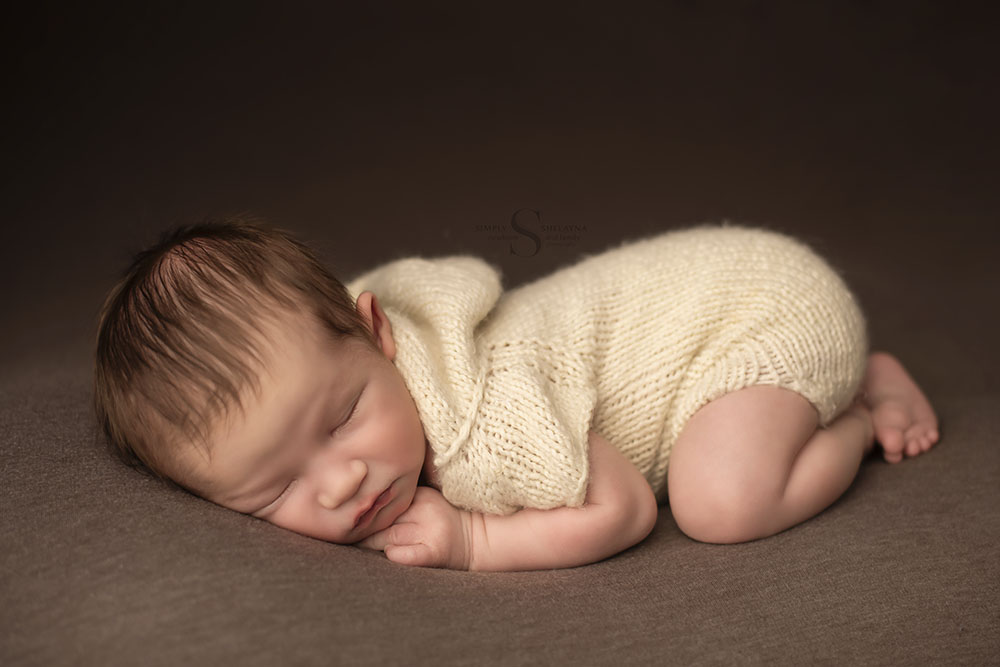 A newborn boy sleeps in bum up pose wearing a hand knitted cream hooded onsie with Simply Shelayna Newborn Photography in Upstate NY.