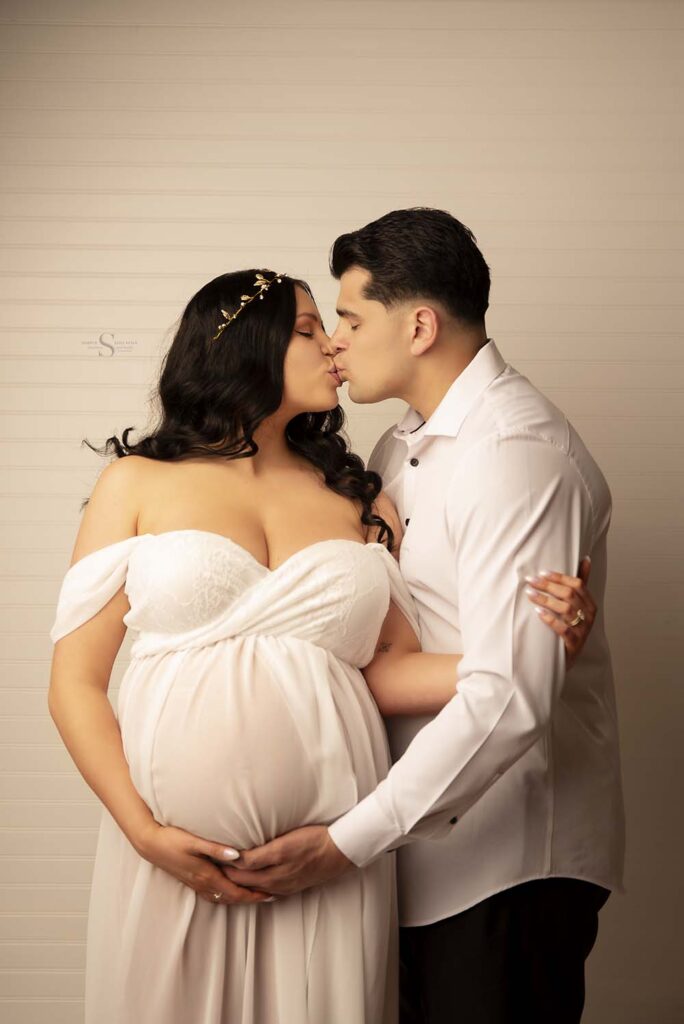 A couple kiss and hold each other close for a maternity portrait with Simply Shelayna Maternity Photography in Oswego NY.