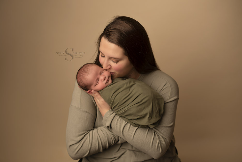 A mother kisses the cheek of her newborn son with Simply Shelayna Newborn Photography in CNY.