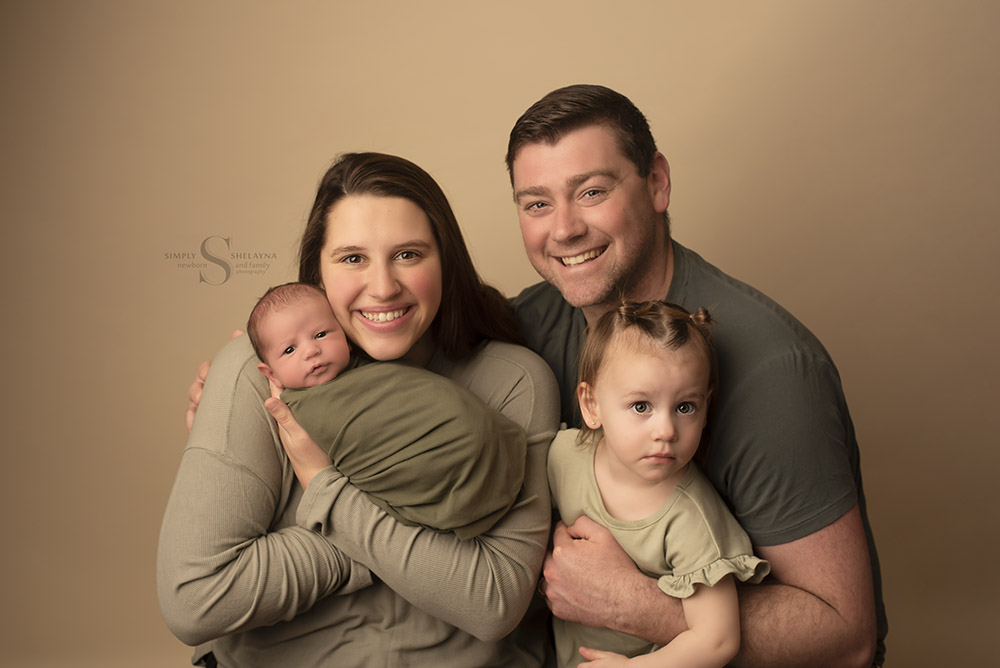 A family of four pose with their newborn son for a family portrait with Simply Shelayna family photographer in Syracuse NY.