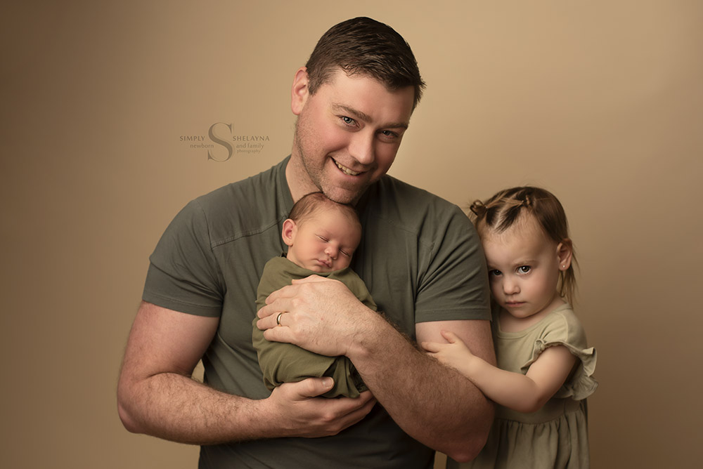 A father holds his infant son for a portrait with Simply Shelayna Newborn Photographer in Syracuse NY.