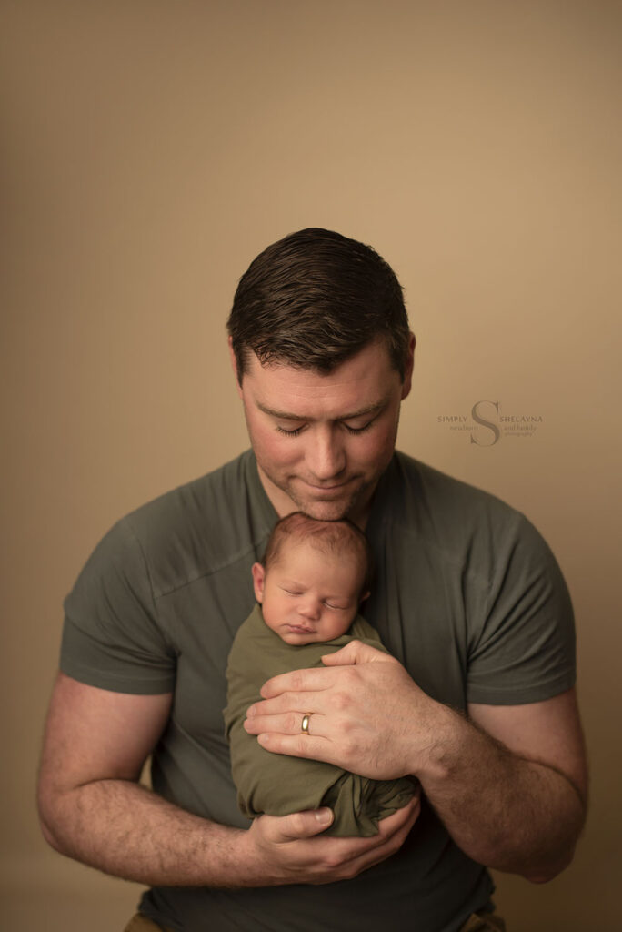 A father holds his infant son for a portrait with Simply Shelayna Newborn Photographer in Syracuse NY.
