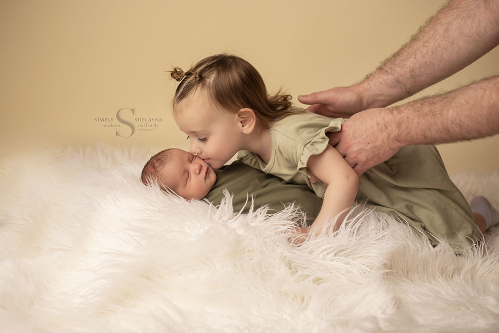 A big sister get's in close to kiss her baby brother on the cheek for a sibling newborn portrait session with Simply Shelayna Newborn Photography in CNY.