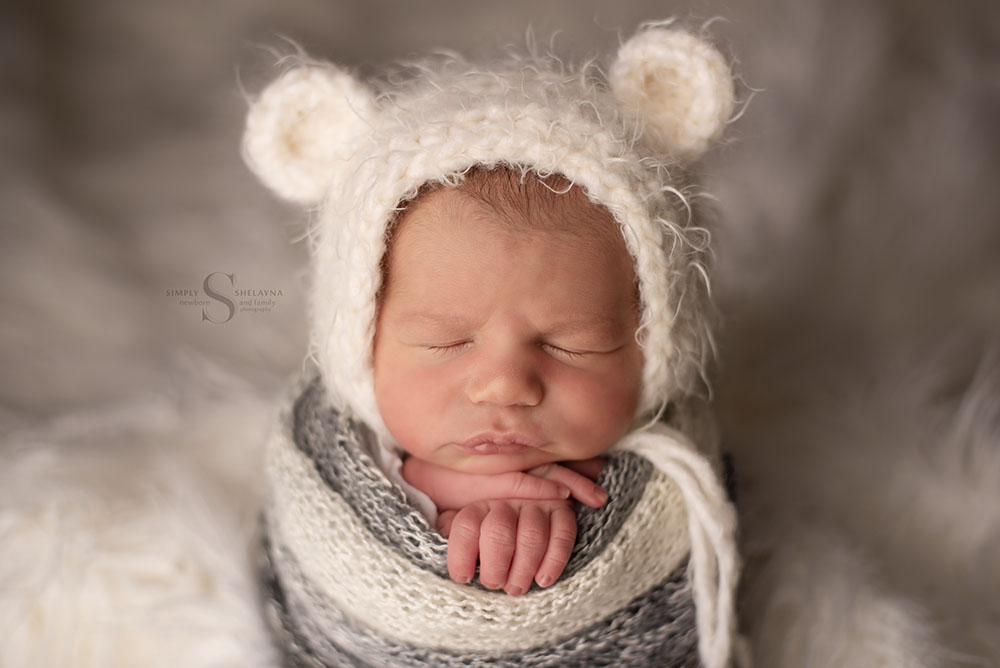 A baby boy wears a teddy bear bonnet for a portrait with Simply Shelayna Newborn photography in Syracuse NY.