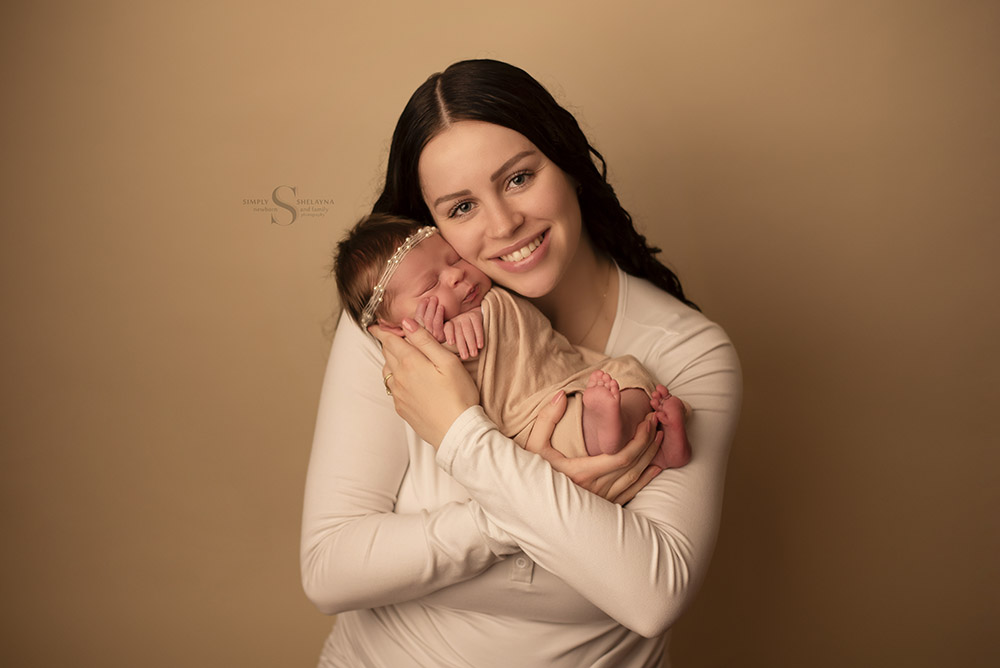 A new mother holds her infant daughter for a portrait with Simply Shelayna Newborn and family photography in Oswego NY.