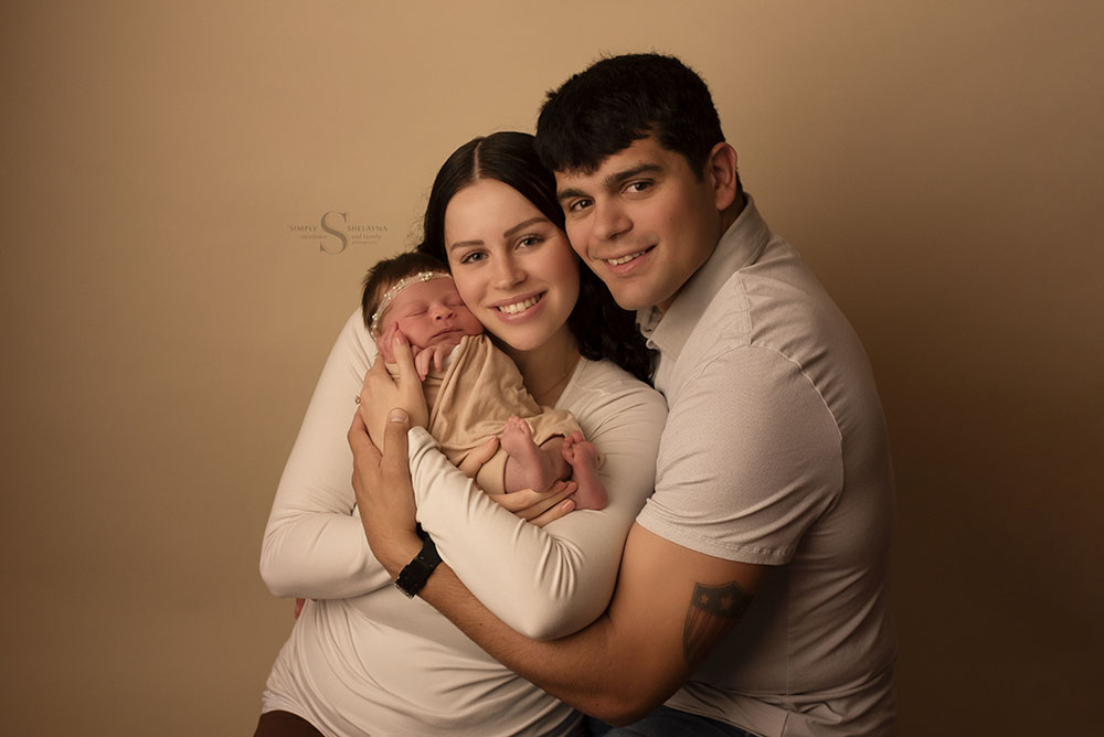 A family of 3 pose with their infant daughter for a portrait with Simply Shelayna Newborn and family photography in Oswego NY.