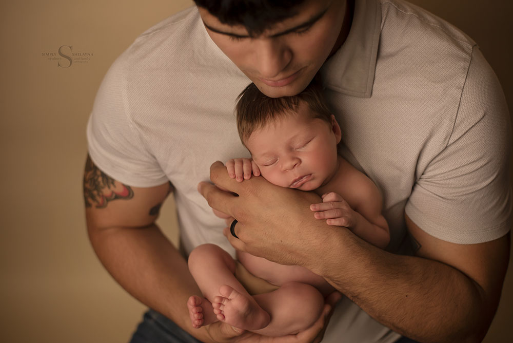 a father holds his infant daughter close to his chest for a newborn portrait with Simply Shelayna Family photography in Syracuse NY.