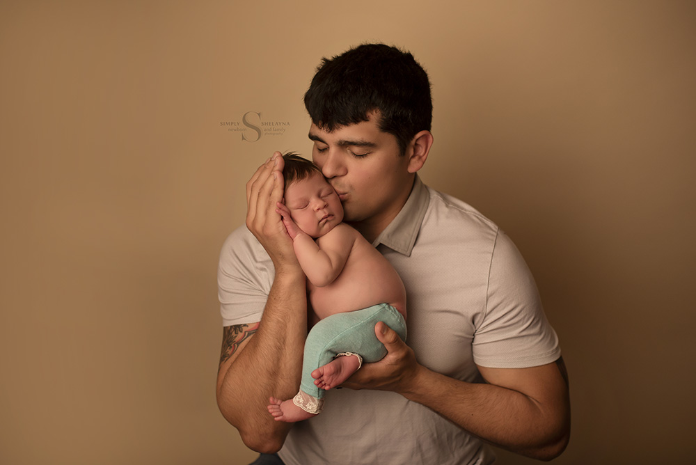 A new father kisses his infant daughter for a portrait with Simply Shelayna Newborn and family photography in Oswego NY.