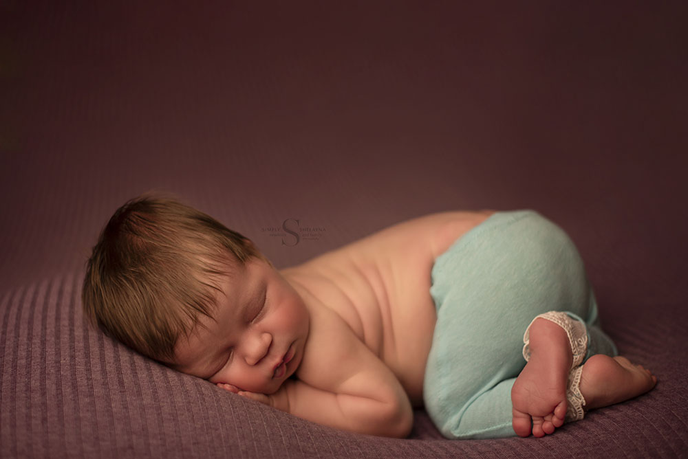 A newborn baby girl wearing teal laced pants sleeps in bum up position for a portrait with Simply Shelayna Newborn Photography in Syracuse NY.