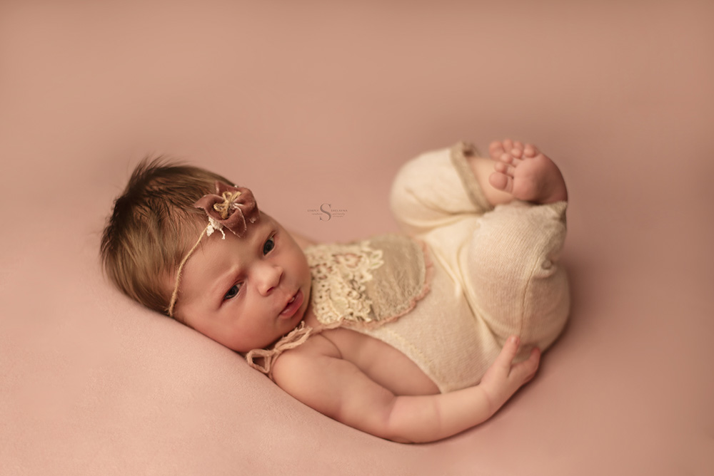 A newborn baby girl lying in huck fin position for a portrait with Simply Shelayna Newborn Photography in Syracuse NY.